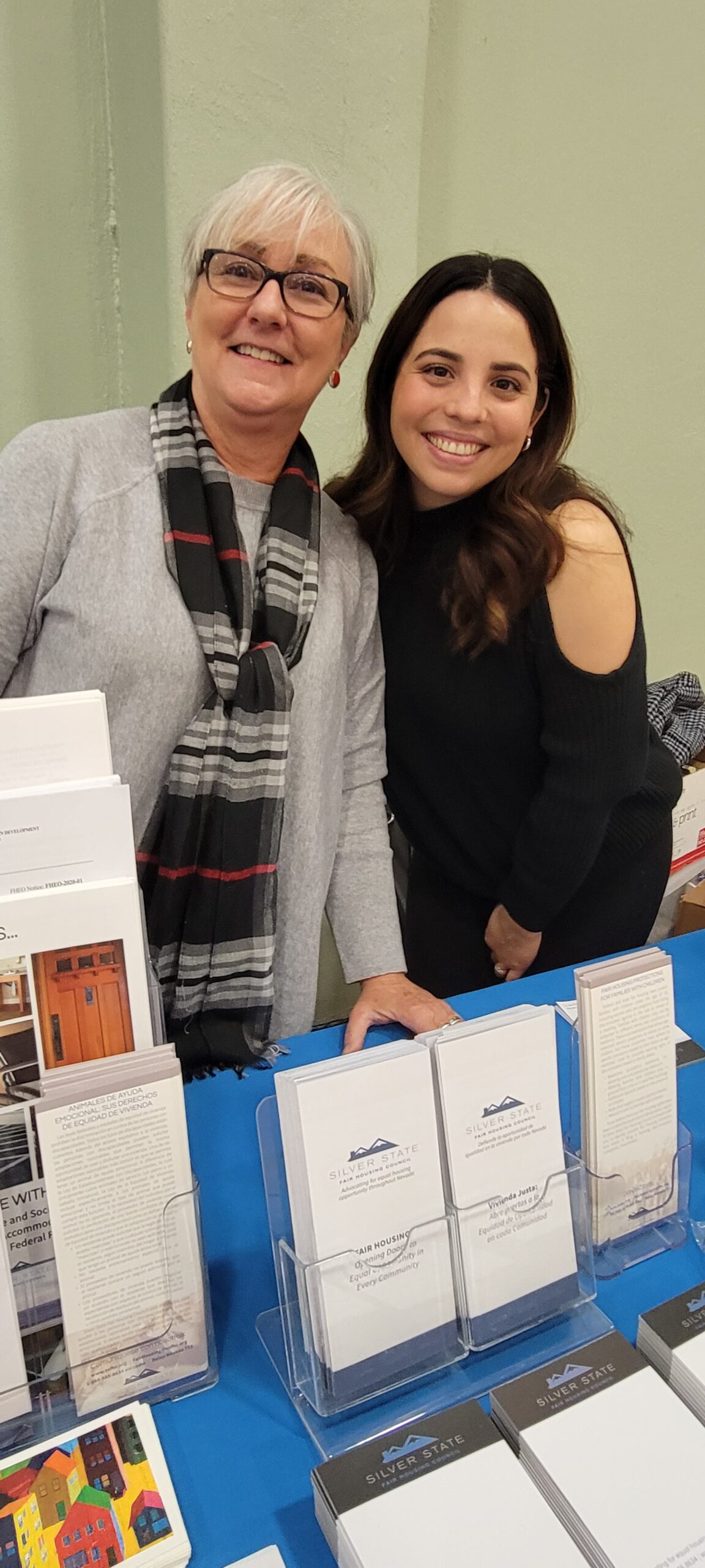 Two women standing in front of a table with books on it.