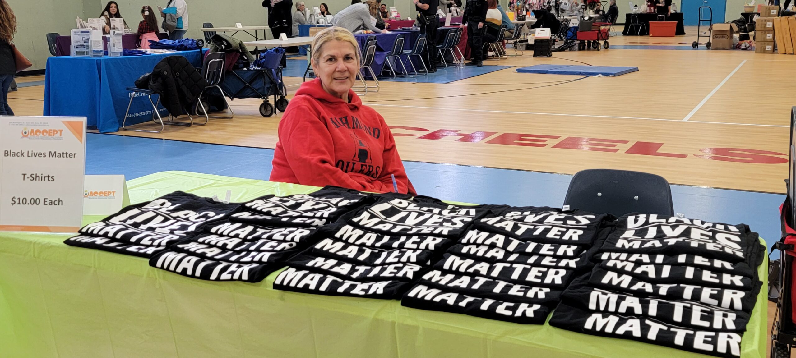 A woman sits at a table with t - shirts on it.