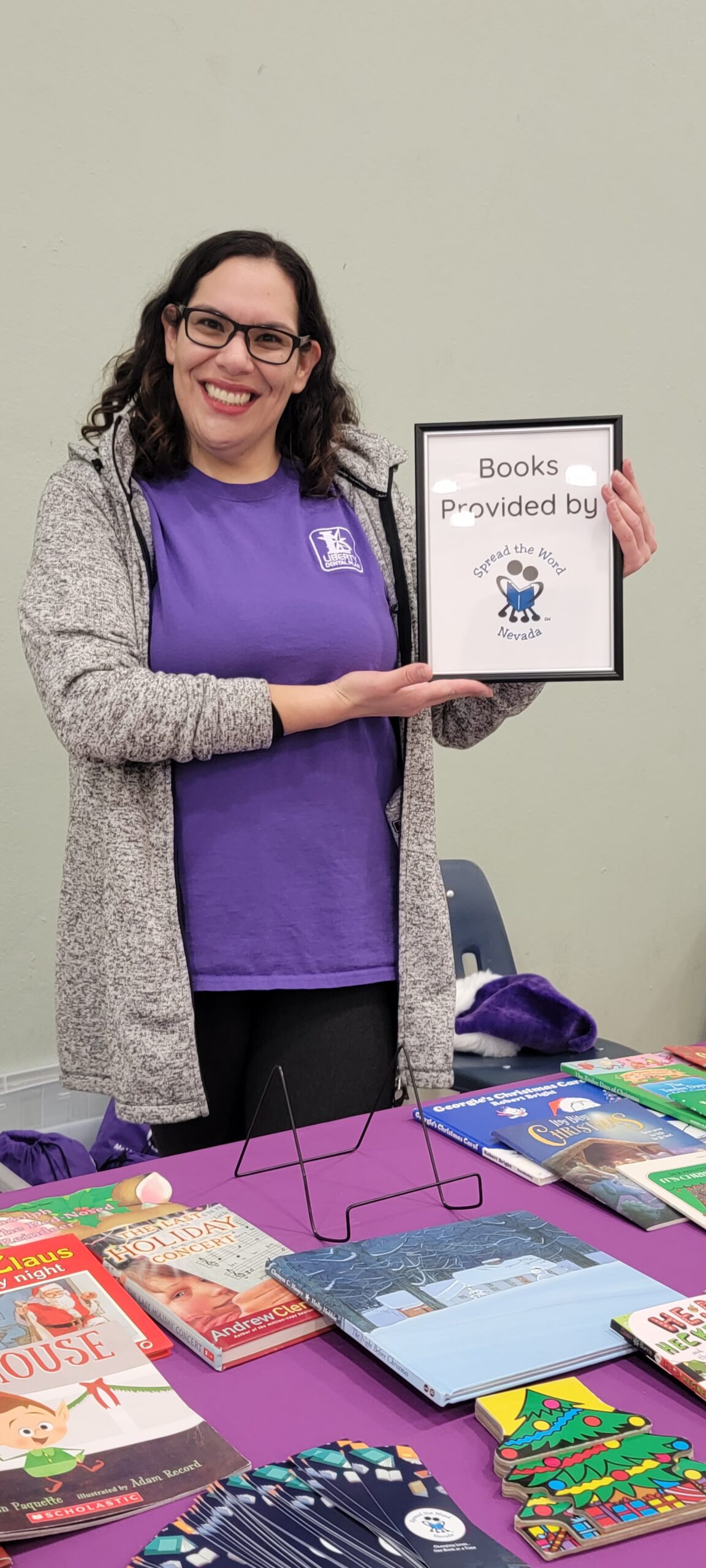A woman holding a purple t shirt and a book on a table.