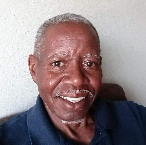 An older man smiling while sitting on a couch.